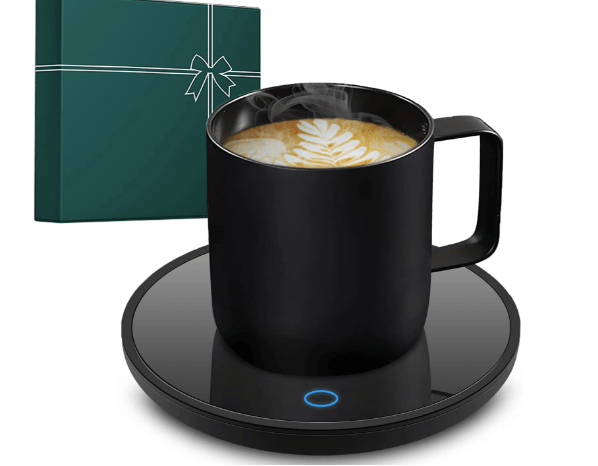 A black coffee mug on a sleek warming plate, with steaming beverage inside, next to a green gift box with a ribbon.