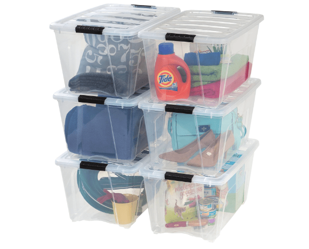 Stacked clear plastic storage bins filled with various items including detergent, towels, and clothing.
