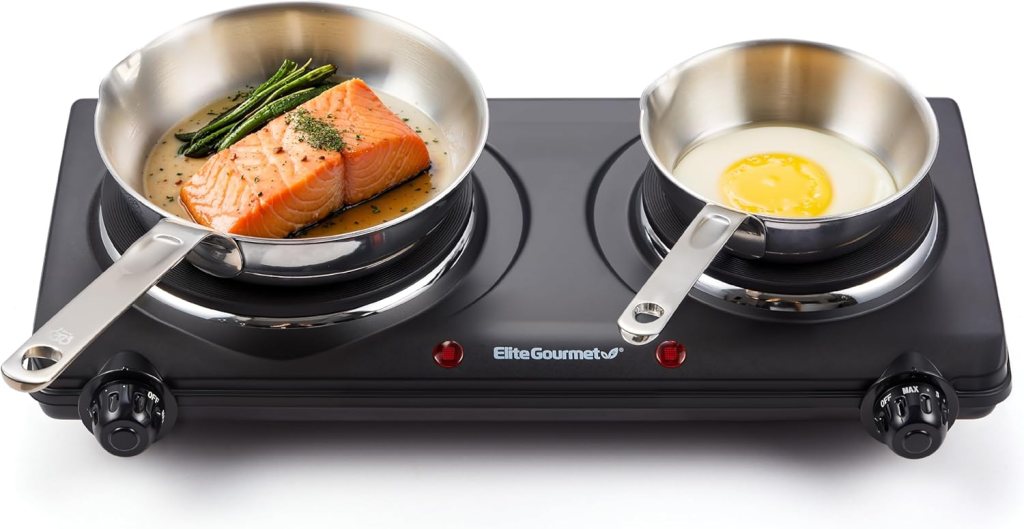 A countertop double electric hot plate with two burners, one featuring a pan of salmon and asparagus, the other holding an egg in a small pot.