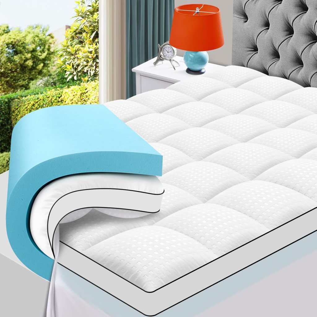 A close-up view of a MASVIS Queen Size Dual Layer Memory Foam Mattress Topper, featuring a blue gel layer on top of a white quilted surface, placed on a bed near a colorful lamp and a window with greenery outside.