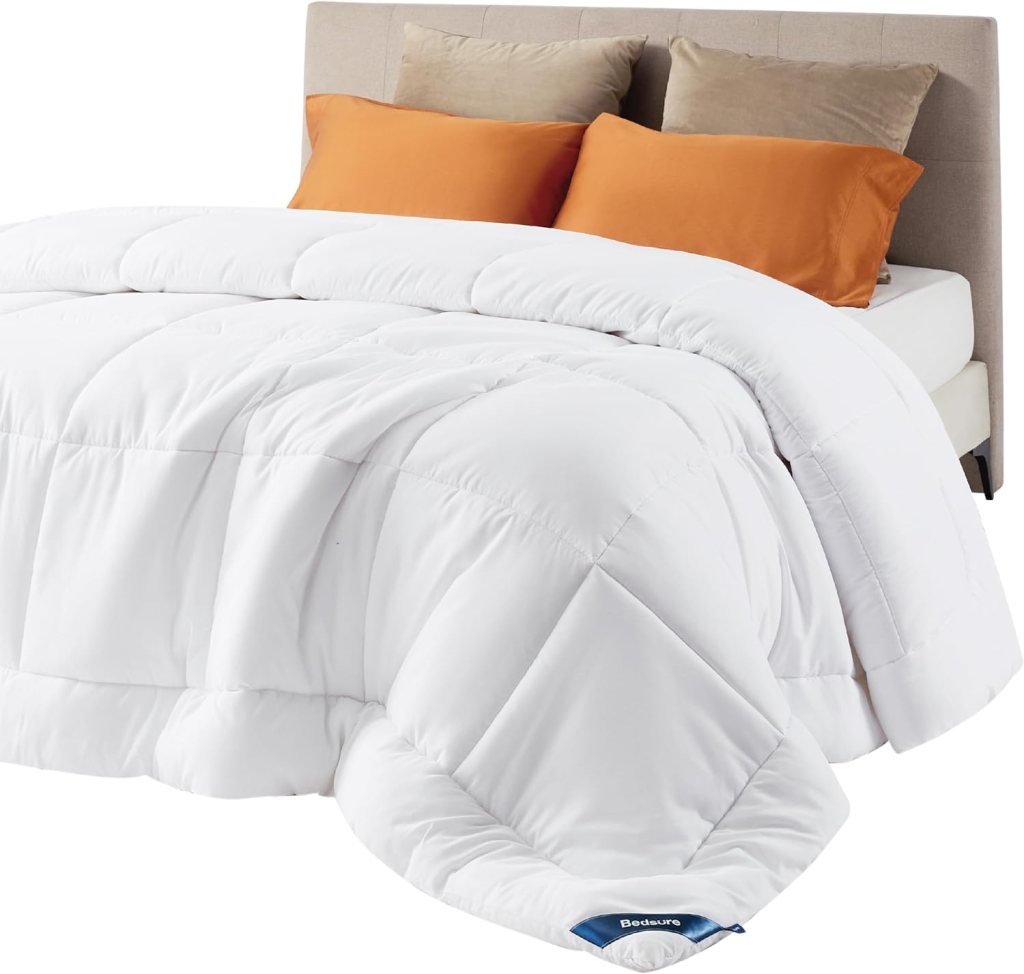 A white quilted comforter is draped over a bed with orange decorative pillows and a beige headboard.