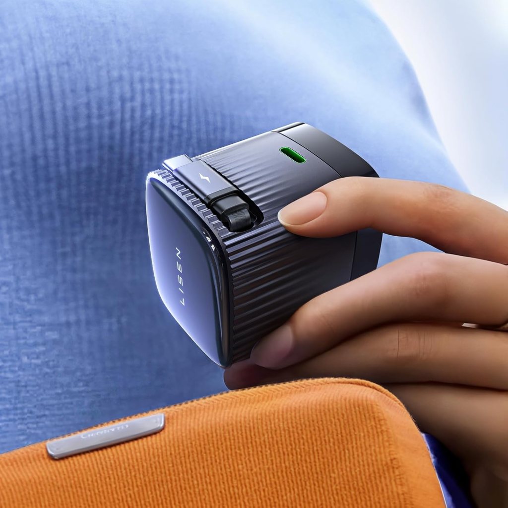 A close-up of a person holding a LISEN retractable phone charger with a textured surface, showing a green indicator light and a dual USB C adapter. The charger is positioned near an orange pouch.
